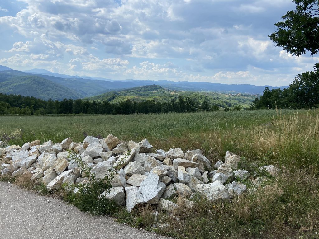 A low-lying pile of stones on a roadside with a line of hills in the background